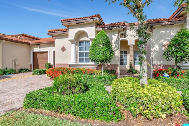 mediterranean / spanish home with an attached garage, a tiled roof, driveway, and stucco siding