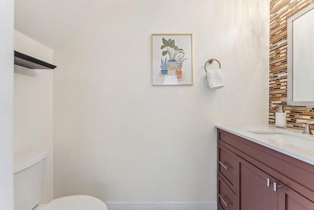 half bathroom with vanity, baseboards, backsplash, and toilet