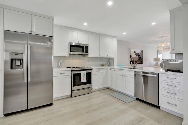 kitchen with appliances with stainless steel finishes, tasteful backsplash, a sink, light countertops, and light wood-type flooring