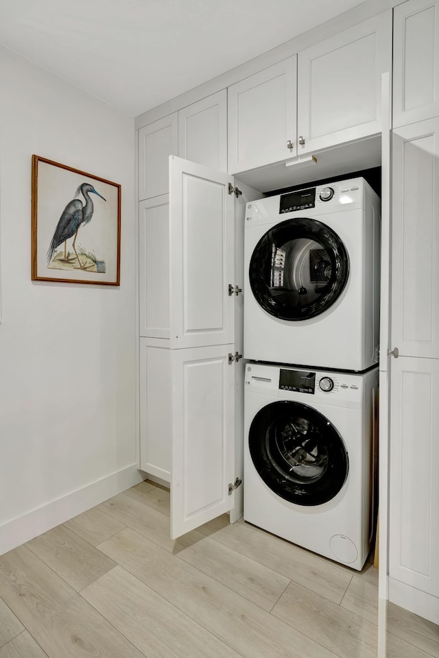 laundry area featuring baseboards, laundry area, stacked washer / dryer, and light wood-style flooring