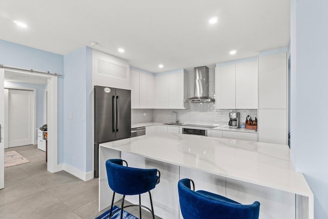 kitchen with wall chimney exhaust hood, a kitchen bar, appliances with stainless steel finishes, a sink, and baseboards