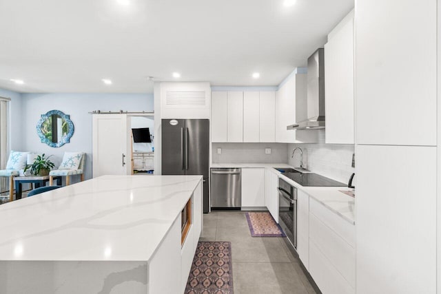 kitchen with white cabinets, wall chimney exhaust hood, a sink, appliances with stainless steel finishes, and a kitchen island