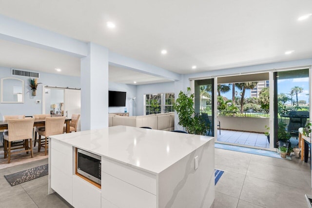 kitchen with visible vents, light tile patterned floors, modern cabinets, stainless steel microwave, and white cabinetry