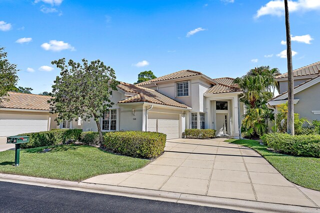 mediterranean / spanish-style house with driveway, a tile roof, a front yard, a garage, and stucco siding