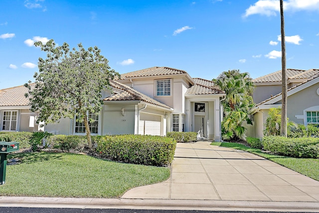 mediterranean / spanish home with a tiled roof, a front lawn, concrete driveway, an attached garage, and stucco siding