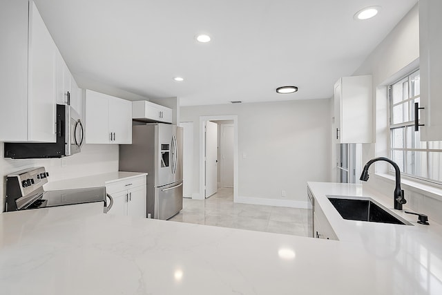 kitchen with light stone countertops, a sink, stainless steel appliances, baseboards, and white cabinetry