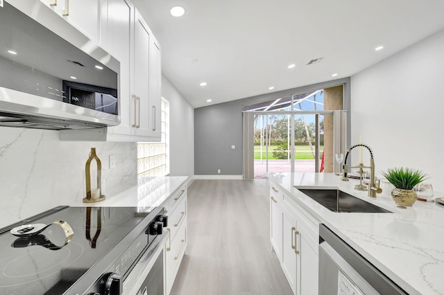 kitchen with stainless steel appliances, a sink, light wood-type flooring, white cabinetry, and light stone countertops