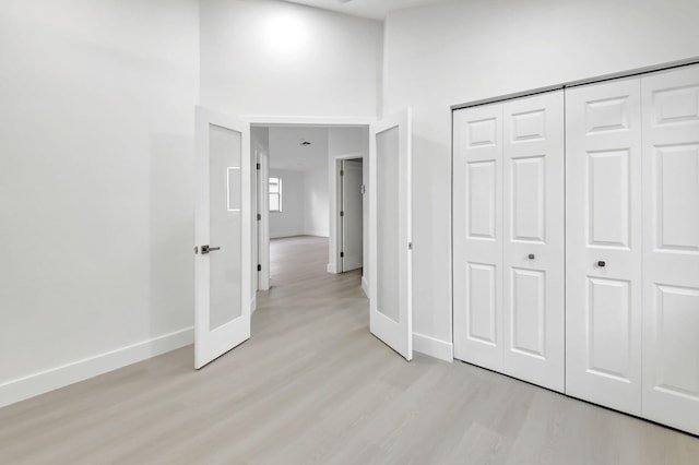unfurnished bedroom featuring light wood-style flooring, baseboards, a high ceiling, and a closet