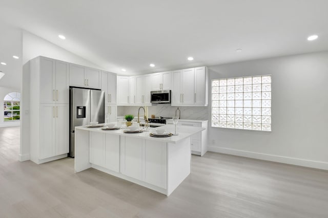 kitchen with a kitchen island with sink, baseboards, light wood-style floors, light countertops, and appliances with stainless steel finishes