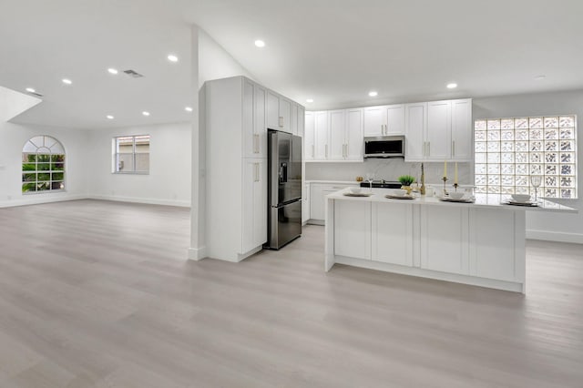 kitchen with a kitchen island with sink, stainless steel microwave, light wood-type flooring, visible vents, and black fridge with ice dispenser