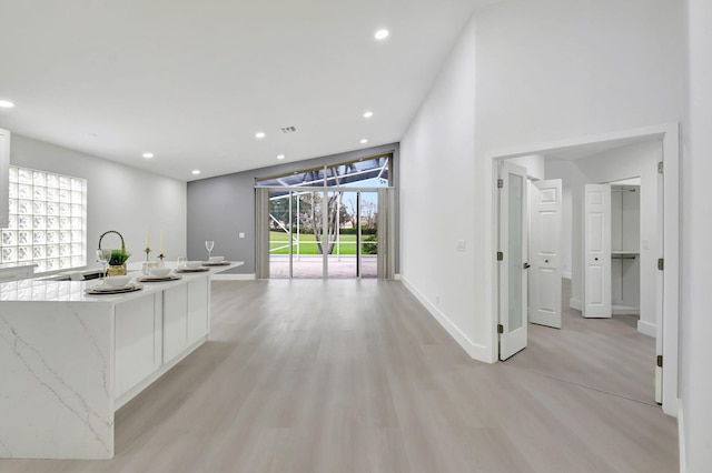 kitchen featuring a kitchen island with sink, light wood-type flooring, baseboards, recessed lighting, and light stone countertops