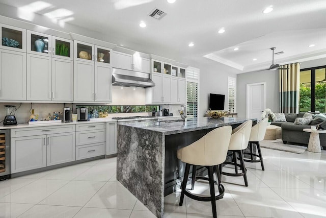 kitchen with a kitchen breakfast bar, light tile patterned floors, under cabinet range hood, visible vents, and a tray ceiling
