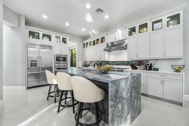kitchen featuring visible vents, built in appliances, light tile patterned floors, and under cabinet range hood