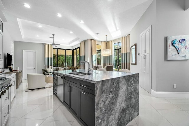 kitchen featuring a raised ceiling, a sink, a kitchen island with sink, light stone countertops, and range