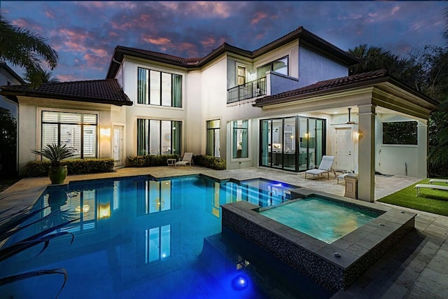 rear view of house featuring a tiled roof, a patio area, stucco siding, and a balcony