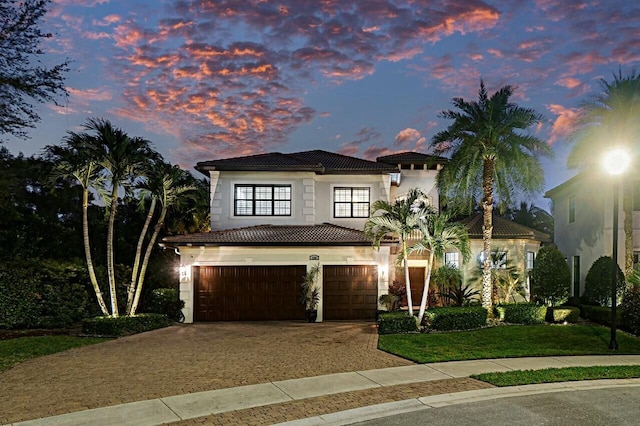mediterranean / spanish-style house featuring stucco siding, driveway, a front yard, a tile roof, and a garage