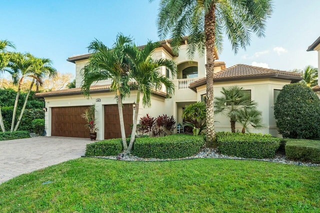 mediterranean / spanish-style house with stucco siding, a front yard, a tile roof, an attached garage, and driveway