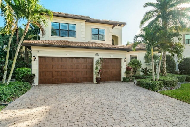 mediterranean / spanish-style home featuring a tile roof, an attached garage, decorative driveway, and stucco siding