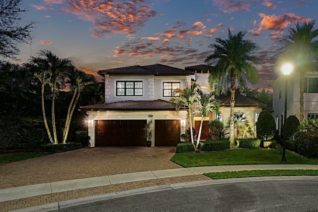 view of front of property featuring a tiled roof, stucco siding, a lawn, a garage, and driveway