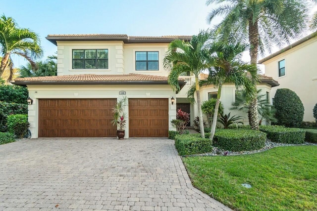 mediterranean / spanish home with stucco siding, decorative driveway, a front lawn, an attached garage, and a tile roof