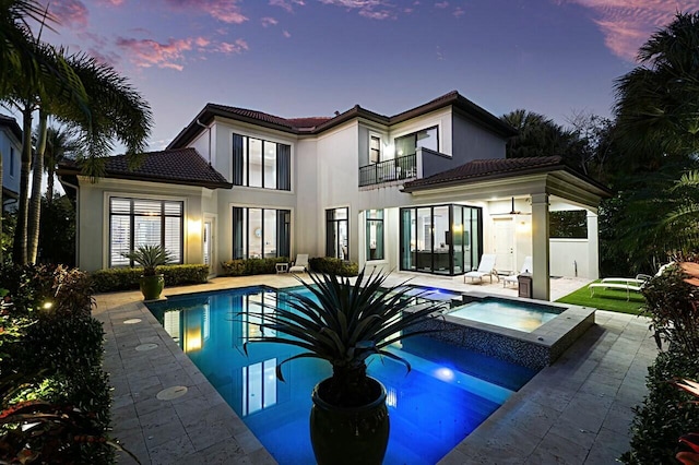 back of house at dusk with a tiled roof, stucco siding, a patio area, and a balcony