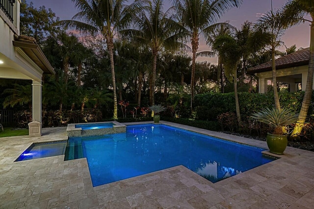 pool at dusk with a patio area and a pool with connected hot tub