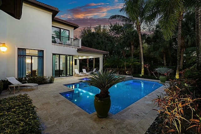 pool at dusk with an outdoor pool and a patio area
