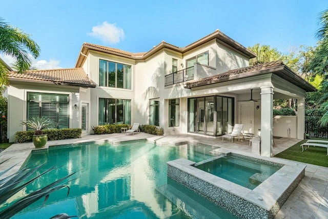 back of house with a tiled roof, a patio area, a pool with connected hot tub, stucco siding, and a balcony