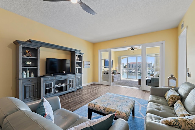 living area featuring wood finished floors, visible vents, a ceiling fan, baseboards, and a textured ceiling
