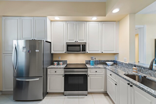 kitchen with a sink, white cabinetry, appliances with stainless steel finishes, light stone counters, and light tile patterned floors