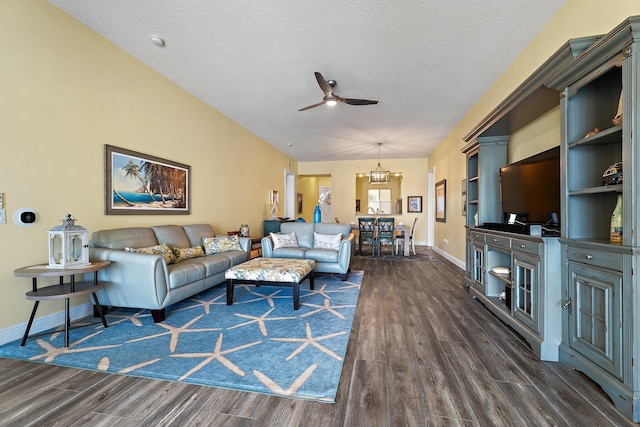 living area with ceiling fan with notable chandelier, baseboards, a textured ceiling, and dark wood finished floors