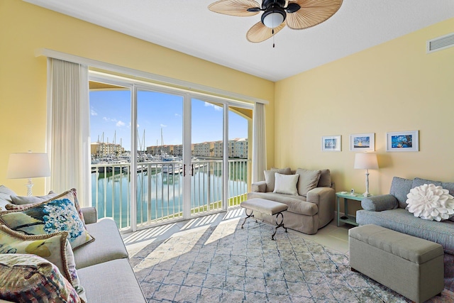 living room featuring tile patterned flooring, a water view, a ceiling fan, and visible vents