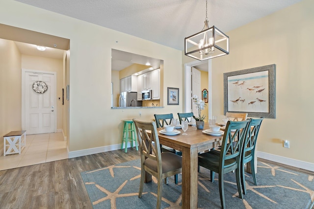 dining space with wood finished floors, baseboards, a textured ceiling, and a chandelier