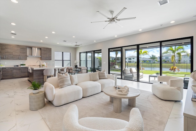 living room featuring recessed lighting, a ceiling fan, light marble finish floors, and a water view