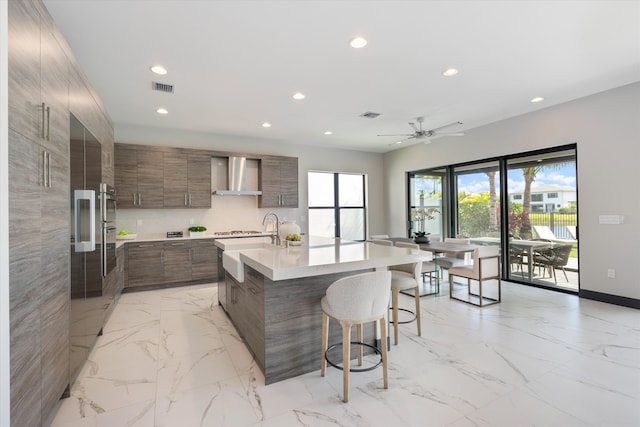kitchen with modern cabinets, wall chimney range hood, recessed lighting, light marble finish floors, and a breakfast bar area