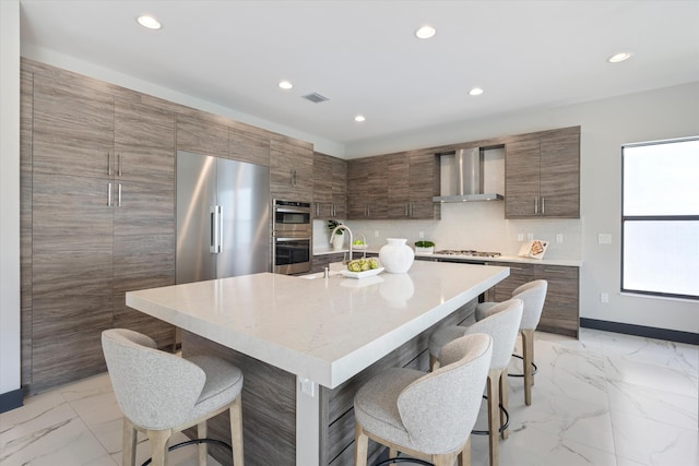 kitchen featuring wall chimney range hood, light marble finish floors, a breakfast bar area, recessed lighting, and stainless steel appliances