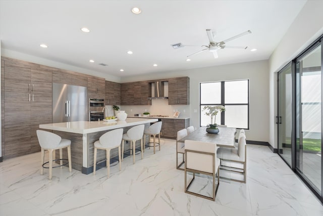 kitchen with wall chimney exhaust hood, a kitchen bar, modern cabinets, appliances with stainless steel finishes, and recessed lighting