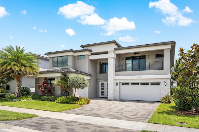 view of front facade with a balcony, stucco siding, an attached garage, decorative driveway, and a front lawn