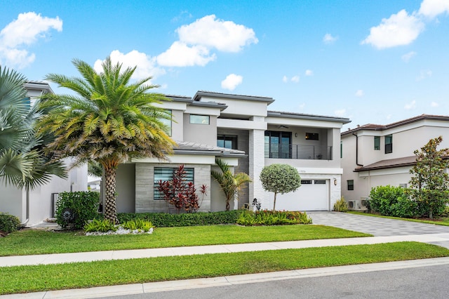 view of front of home with a balcony, an attached garage, driveway, stucco siding, and a front lawn