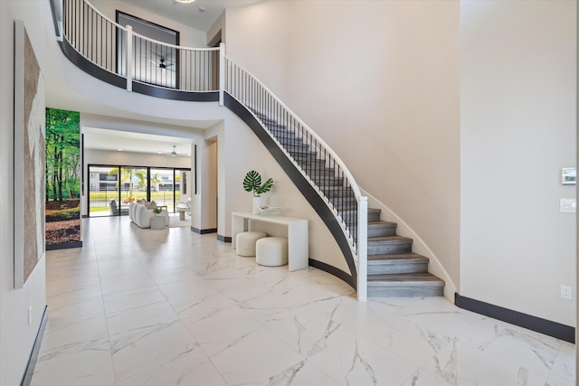 stairs featuring baseboards, marble look tile flooring, and a high ceiling