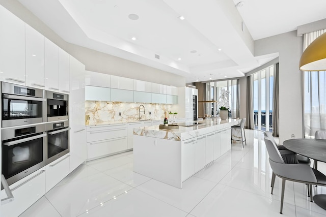 kitchen featuring modern cabinets, a sink, a spacious island, backsplash, and stainless steel double oven