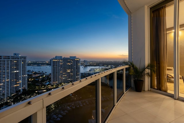 balcony at dusk featuring a water view and a view of city