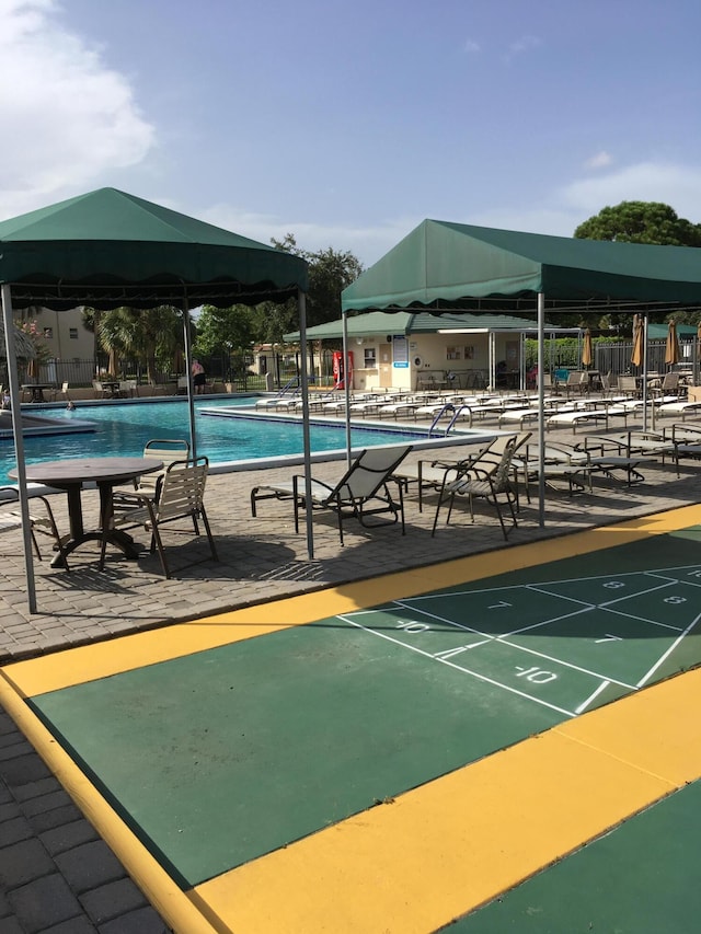 view of property's community with a swimming pool, fence, and shuffleboard