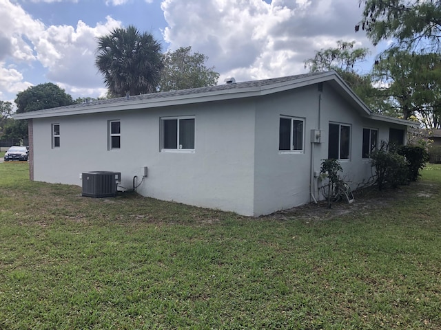 view of side of property with stucco siding, central AC unit, and a lawn