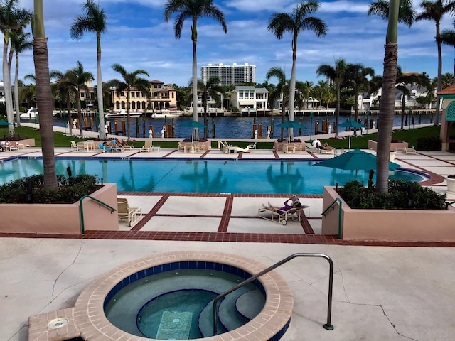 community pool featuring a water view, a patio, and a hot tub