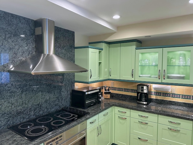 kitchen with tasteful backsplash, green cabinets, black electric stovetop, and wall chimney range hood