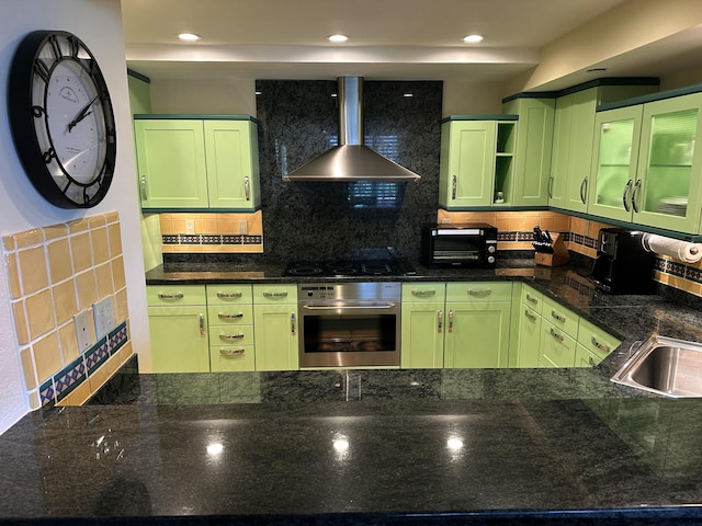 kitchen with stainless steel oven, black electric cooktop, green cabinetry, and wall chimney range hood