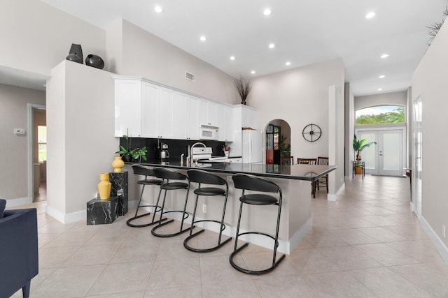 19699 Dinner Key Dr, Boca Raton, FL 33498 - kitchen featuring dark countertops, white appliances, light tile patterned flooring, arched walkways, and a peninsula