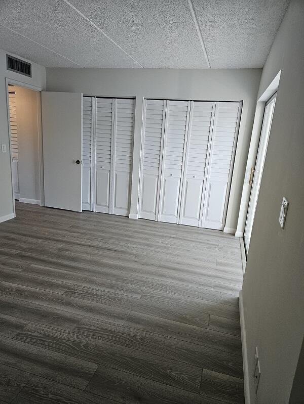 300 Village Green Cir S Unit 206, Palm Springs, FL 33461 - unfurnished bedroom with wood finished floors, a textured ceiling, two closets, baseboards, and visible vents