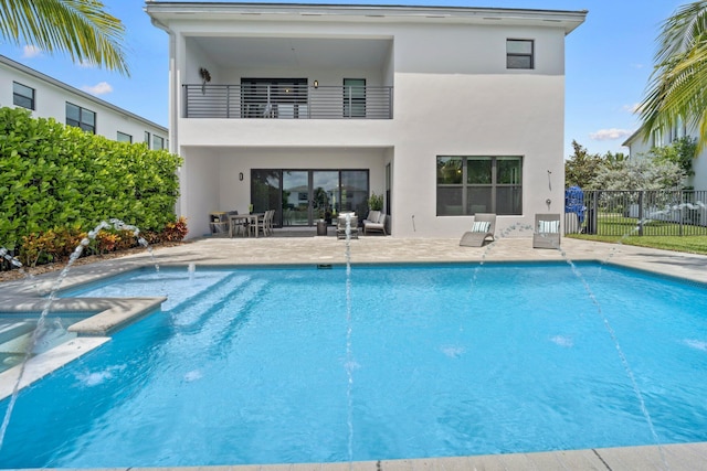 rear view of property with fence, stucco siding, a fenced in pool, and a balcony